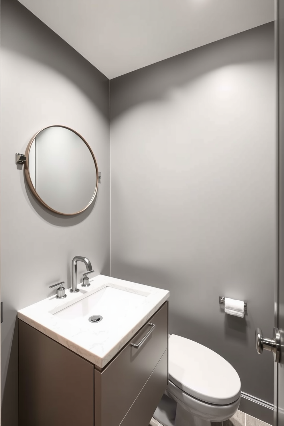 A modern powder room featuring sleek lines and a minimalist aesthetic. The walls are adorned with a soft gray hue, complemented by a floating vanity with a white quartz countertop. Subtle metallic accents are integrated throughout the space, including brushed nickel fixtures and decorative hardware. A round mirror with a thin metallic frame hangs above the vanity, enhancing the room's sophisticated vibe.