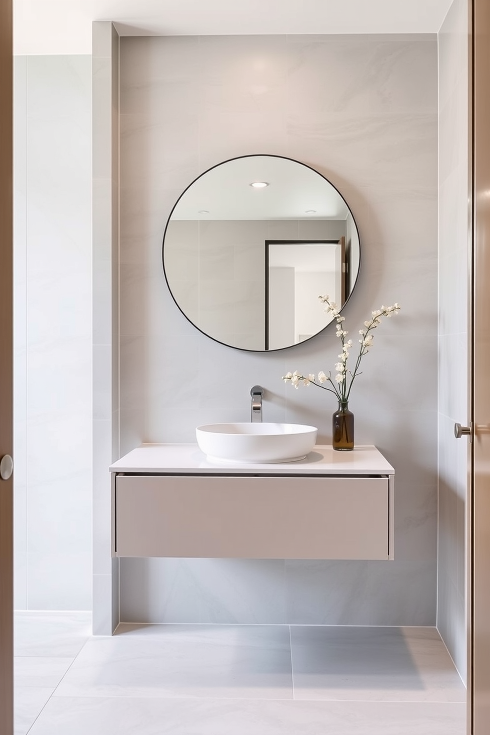 A sleek floating vanity with clean lines complements the open space, creating a sense of airiness. The vanity features a quartz countertop and minimalist hardware, enhancing the contemporary aesthetic. The walls are adorned with light gray tiles that extend to the ceiling, providing a seamless look. A large round mirror hangs above the vanity, reflecting natural light and adding depth to the modern powder room.