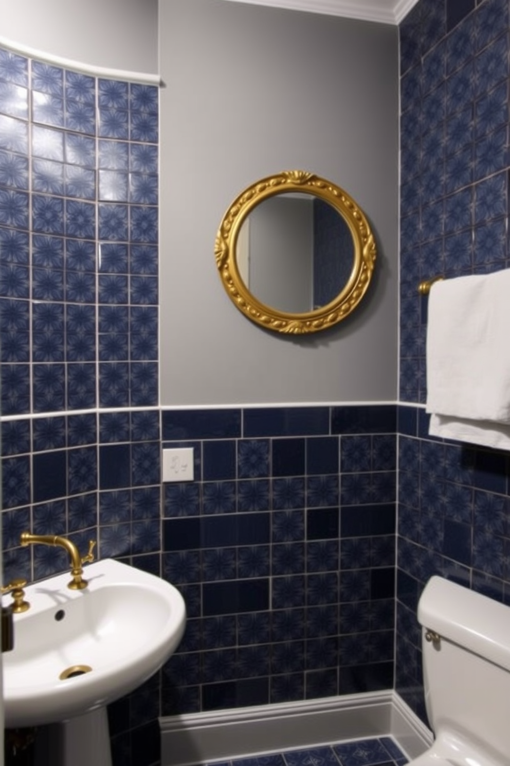 A moody powder room featuring deep blue tiles adorned with intricate patterns that create a captivating visual impact. The walls are painted in a complementary soft gray, enhancing the richness of the tiles while maintaining a cozy atmosphere. A sleek white pedestal sink sits against one wall, with a vintage gold faucet that adds a touch of elegance. Above the sink, a round mirror with a decorative gold frame reflects the beautiful tile work, creating an inviting focal point in the space.