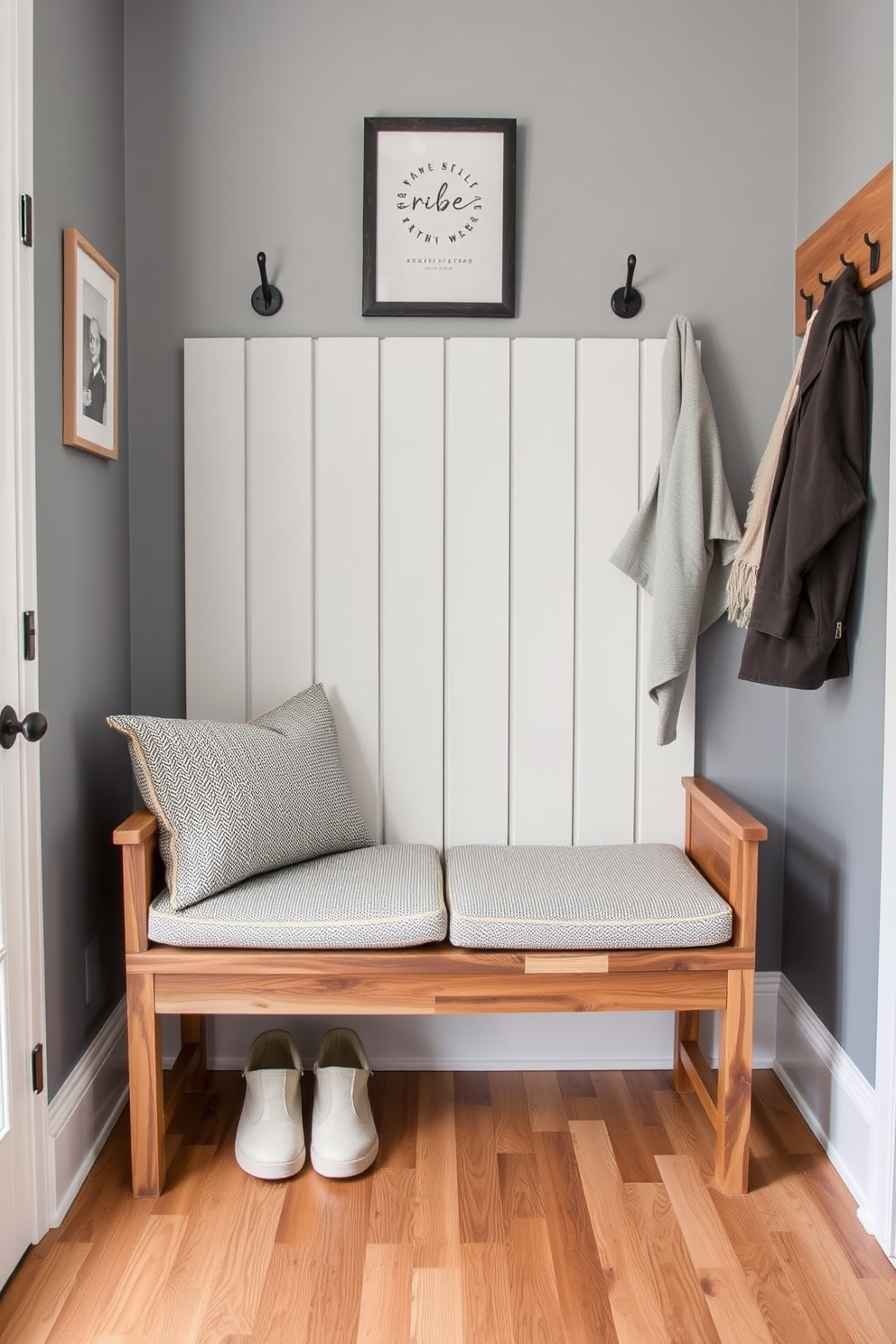 A stylish mudroom features a bench crafted from a blend of rich wood and sleek metal. The bench is adorned with plush cushions in a neutral tone, providing comfort and elegance to the entryway. Above the bench, hooks made of brushed metal are mounted on a wooden panel, perfect for hanging coats and bags. The floor is covered with a durable, patterned rug that adds a touch of color and warmth to the space.