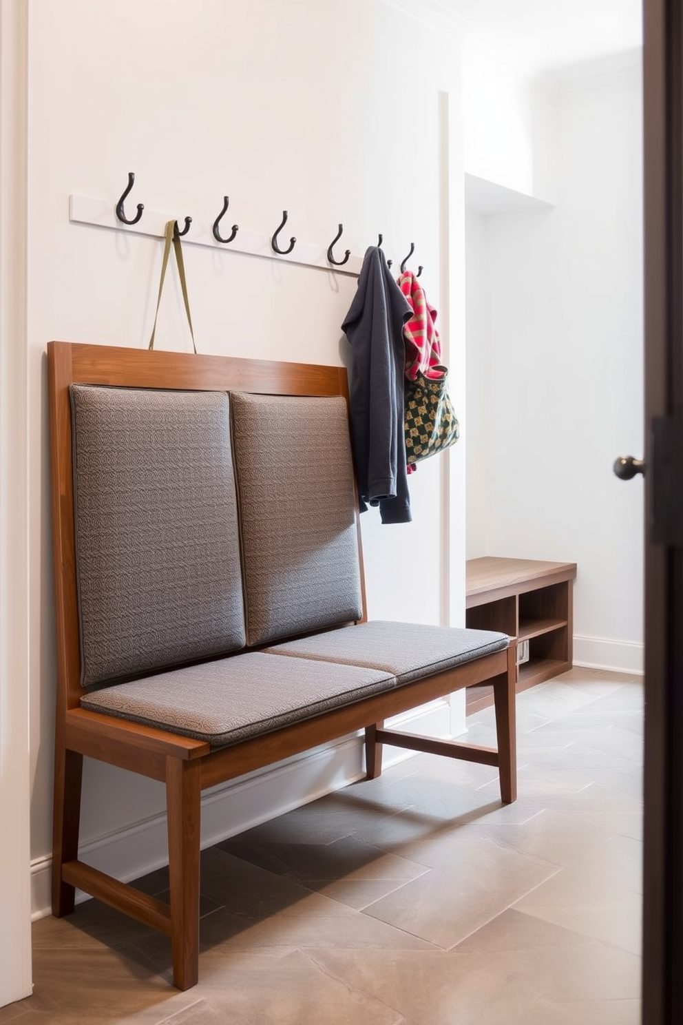 A cozy mudroom featuring a bench with a soft cushion and elegant armrests. The bench is positioned against a wall adorned with hooks for coats and a stylish rug beneath it, creating a welcoming entryway.