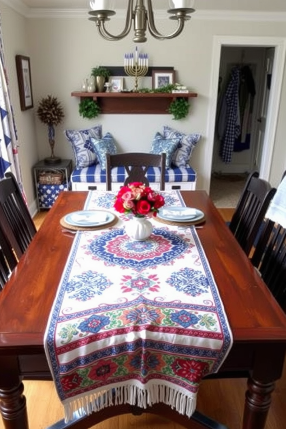 A beautifully set dining table features a vibrant table runner adorned with traditional patterns in rich colors. The runner cascades elegantly over a polished wooden table, enhancing the overall warmth of the dining space. The mudroom is adorned with festive Hanukkah decorations, including a menorah displayed prominently on a shelf. Cozy blue and white accents, such as pillows and throws, create an inviting atmosphere for family gatherings during the holiday season.