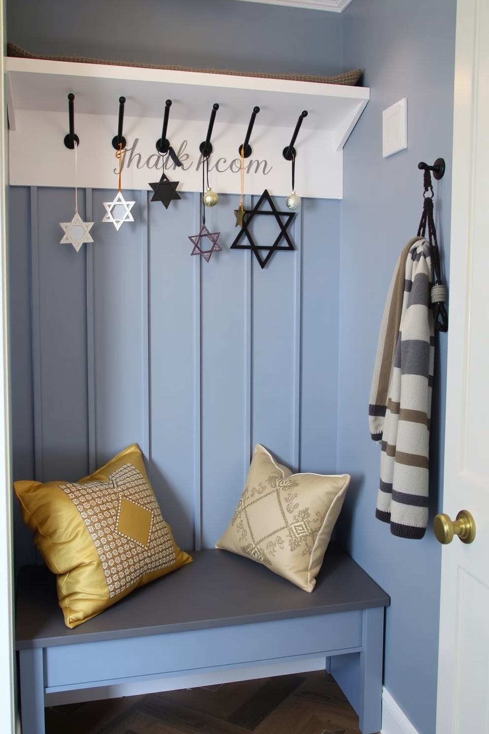 A cozy mudroom adorned for Hanukkah features hooks from which Star of David ornaments dangle gracefully. The walls are painted a soft blue, and a welcoming bench is lined with festive throw pillows in shades of gold and silver.