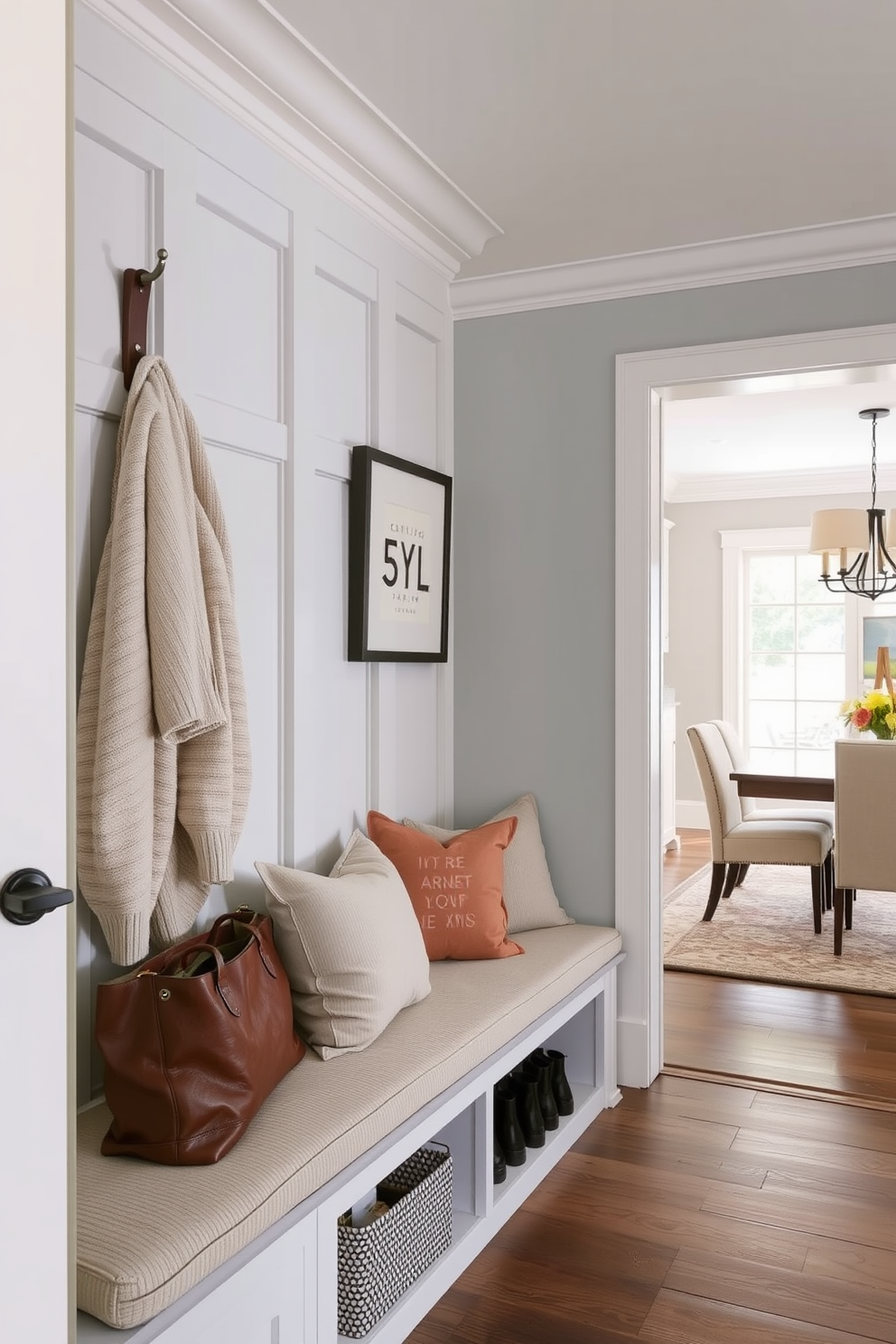 A stylish mudroom features a wall-mounted bench adorned with plush cushions in a soft neutral tone. The space is designed with built-in storage for shoes and bags, seamlessly connecting to the dining room through an open layout.