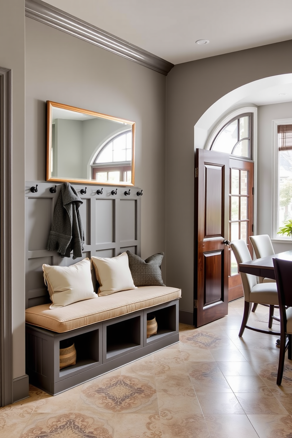 A stylish mudroom adjacent to the dining room features a built-in bench with plush cushions and hooks for coats. The walls are painted in a soft gray, and the floor is covered with a durable yet elegant tile that complements the overall design. A large mirror hangs above the bench, providing a perfect spot for last-minute outfit checks. Natural light floods the space through a nearby window, enhancing the inviting atmosphere of this functional entryway.