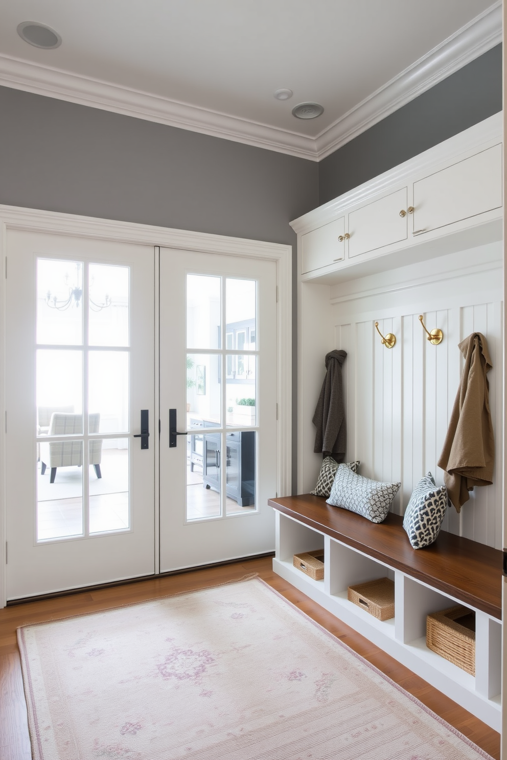 A bright and airy mudroom features elegant glass doors that provide stylish visibility into the adjoining family room. The space is adorned with built-in storage benches, hooks for coats, and a soft area rug that adds warmth to the entryway.