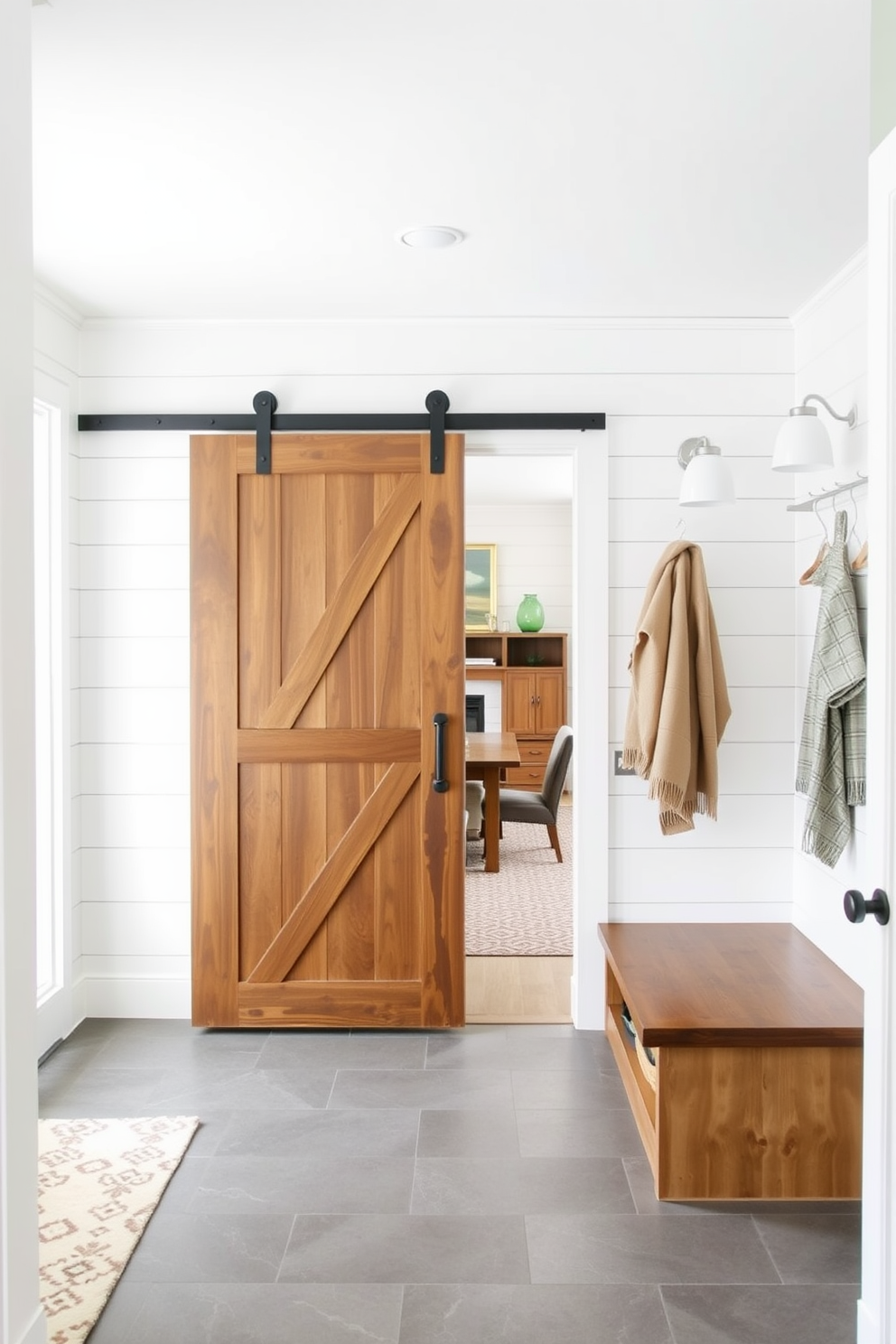 A modern mudroom featuring a sliding barn door that elegantly separates the space from the family room. The walls are adorned with shiplap, and the floor is covered with durable tile for easy maintenance. Cozy built-in benches with storage underneath provide a functional yet stylish seating area. Bright lighting fixtures enhance the welcoming atmosphere, making the mudroom both practical and inviting.