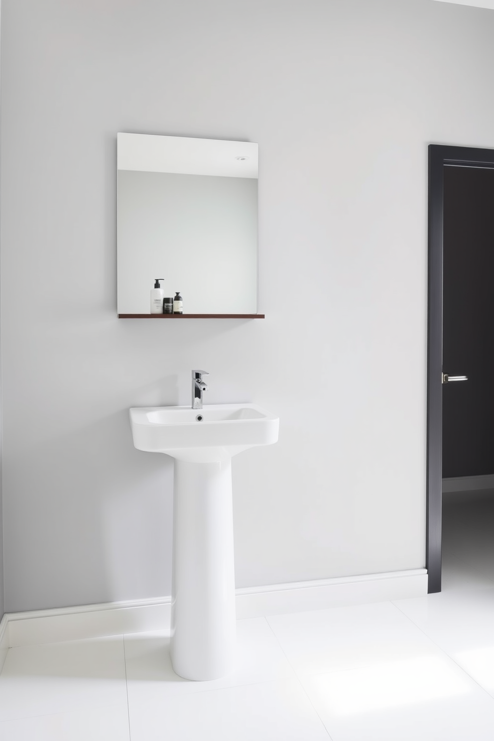 A minimalist bathroom design featuring a sleek white pedestal sink with a single modern faucet. The walls are painted in a soft gray tone, and the floor is adorned with large white tiles for a clean look. To maximize space, a narrow floating shelf is mounted above the sink, displaying a few essential toiletries. A large frameless mirror reflects the natural light coming in from a small window, enhancing the airy feel of the room.