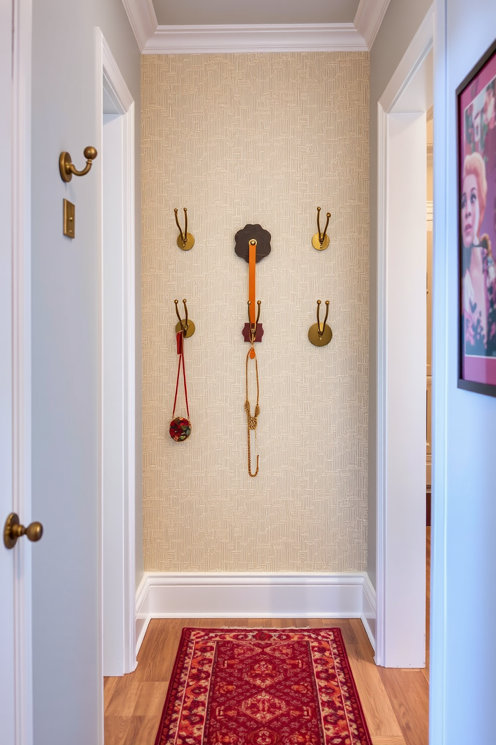 A narrow entryway features a series of stylish coat hooks arranged on a textured wall. Each hook is uniquely designed, combining materials like brass and wood to create a visually appealing focal point. The floor is adorned with a chic runner rug that complements the color scheme of the entryway. Soft lighting illuminates the space, enhancing the decorative elements and making the area feel inviting.