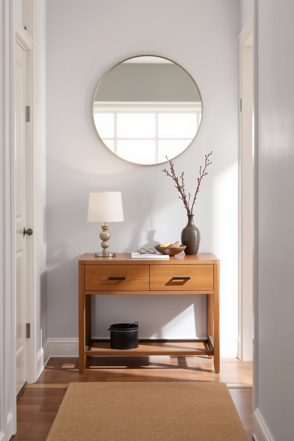 A functional entryway table with drawers is positioned against a light gray wall. The table features a sleek design with a warm wood finish and is adorned with a small decorative lamp and a bowl for keys. Above the table, a large round mirror reflects natural light, enhancing the space. A stylish rug in neutral tones lies underfoot, adding warmth to the narrow entryway.