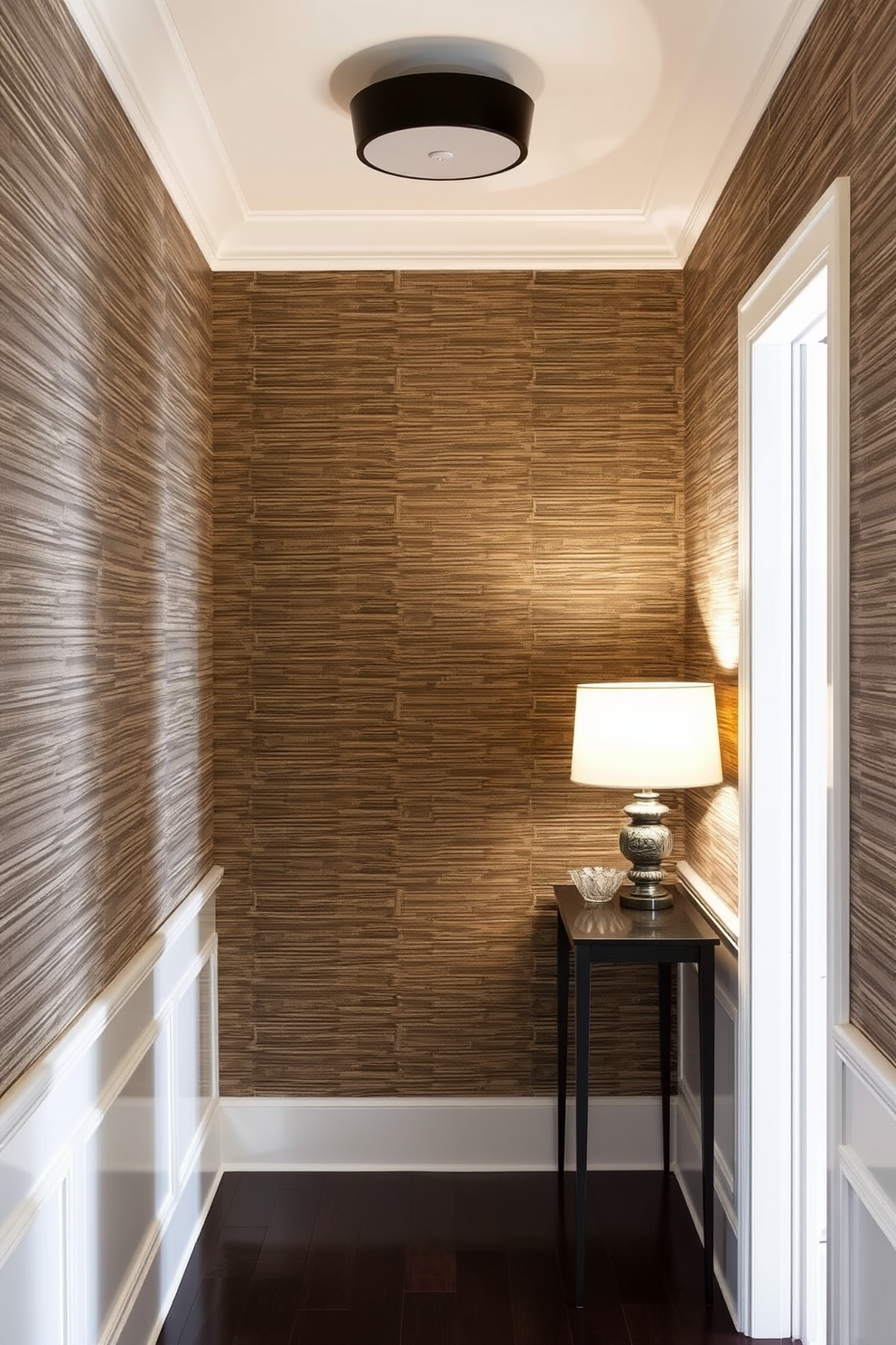 A narrow foyer adorned with textured wallpaper that adds depth and visual interest. The space features a slim console table against one wall, topped with a stylish lamp and a small decorative bowl.