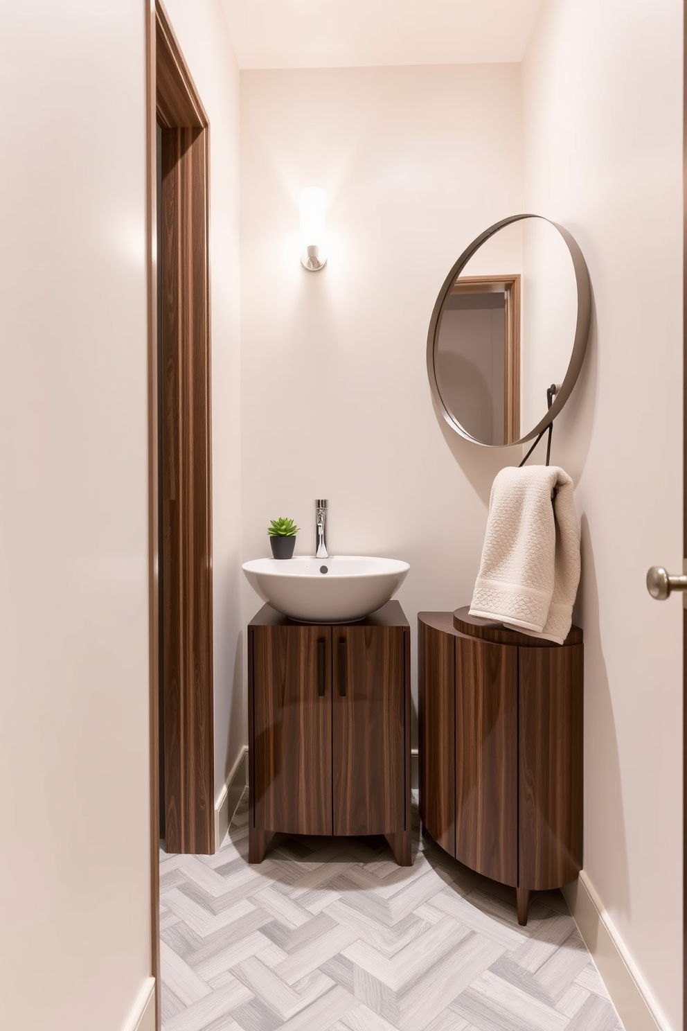 A narrow powder room featuring a sleek small cabinet for storage, finished in a rich walnut wood that complements the overall design. The walls are adorned with a soft cream paint, and the floor showcases elegant herringbone tiles in a light gray tone. A stylish pedestal sink occupies one corner, paired with a round mirror that reflects the ambient lighting from a modern wall sconce. Decorative accents include a small potted plant on the cabinet and a plush hand towel neatly arranged on a nearby hook.