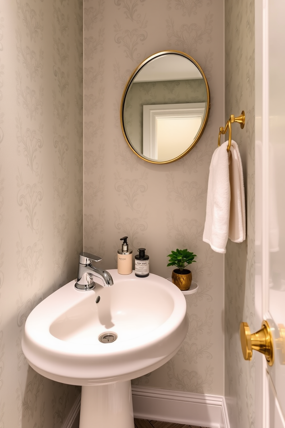 A narrow powder room features a sleek pedestal sink with a polished chrome faucet. The walls are adorned with elegant wallpaper in a soft pastel hue, complemented by a decorative towel rack made of brushed gold. A round mirror with a delicate frame hangs above the sink, reflecting the stylish ambiance. The floor is covered in a chic herringbone pattern, and a small potted plant adds a touch of greenery to the space.