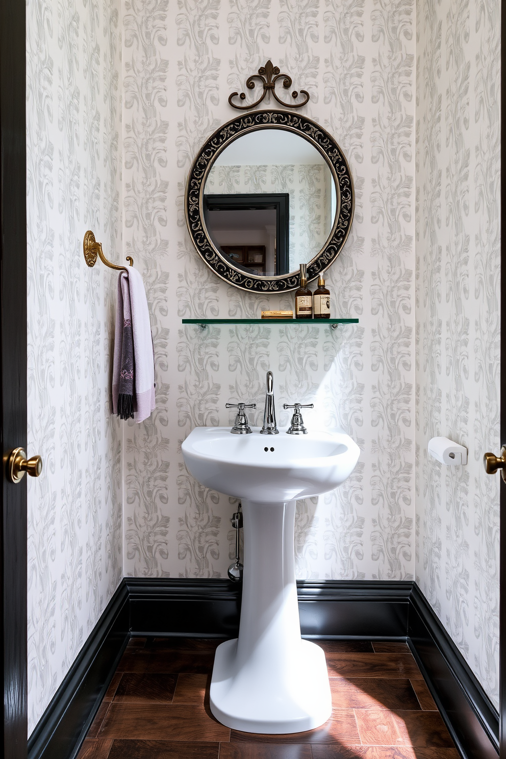 A narrow powder room featuring a sleek pedestal sink with a polished chrome faucet. The walls are adorned with elegant wallpaper in a soft pastel hue, and there are stylish hooks for towels and accessories mounted beside the sink. The floor is finished with dark wood planks that contrast beautifully with the light walls. A round mirror with a decorative frame hangs above the sink, complemented by a small shelf for decorative items and essentials.