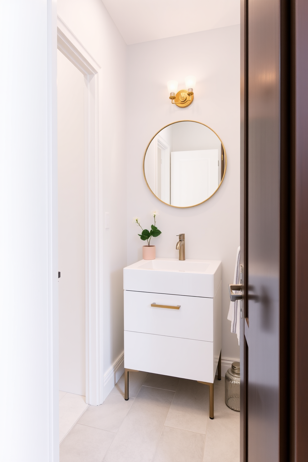 A narrow powder room design featuring light-colored walls to create an airy and spacious feel. The floor is adorned with light gray tiles, and a sleek white vanity with a minimalist sink is positioned against one wall. Above the vanity, a round mirror with a thin gold frame reflects the soft lighting from a stylish wall sconce. Decorative elements like a small potted plant and elegant hand towels add a touch of sophistication to the overall design.