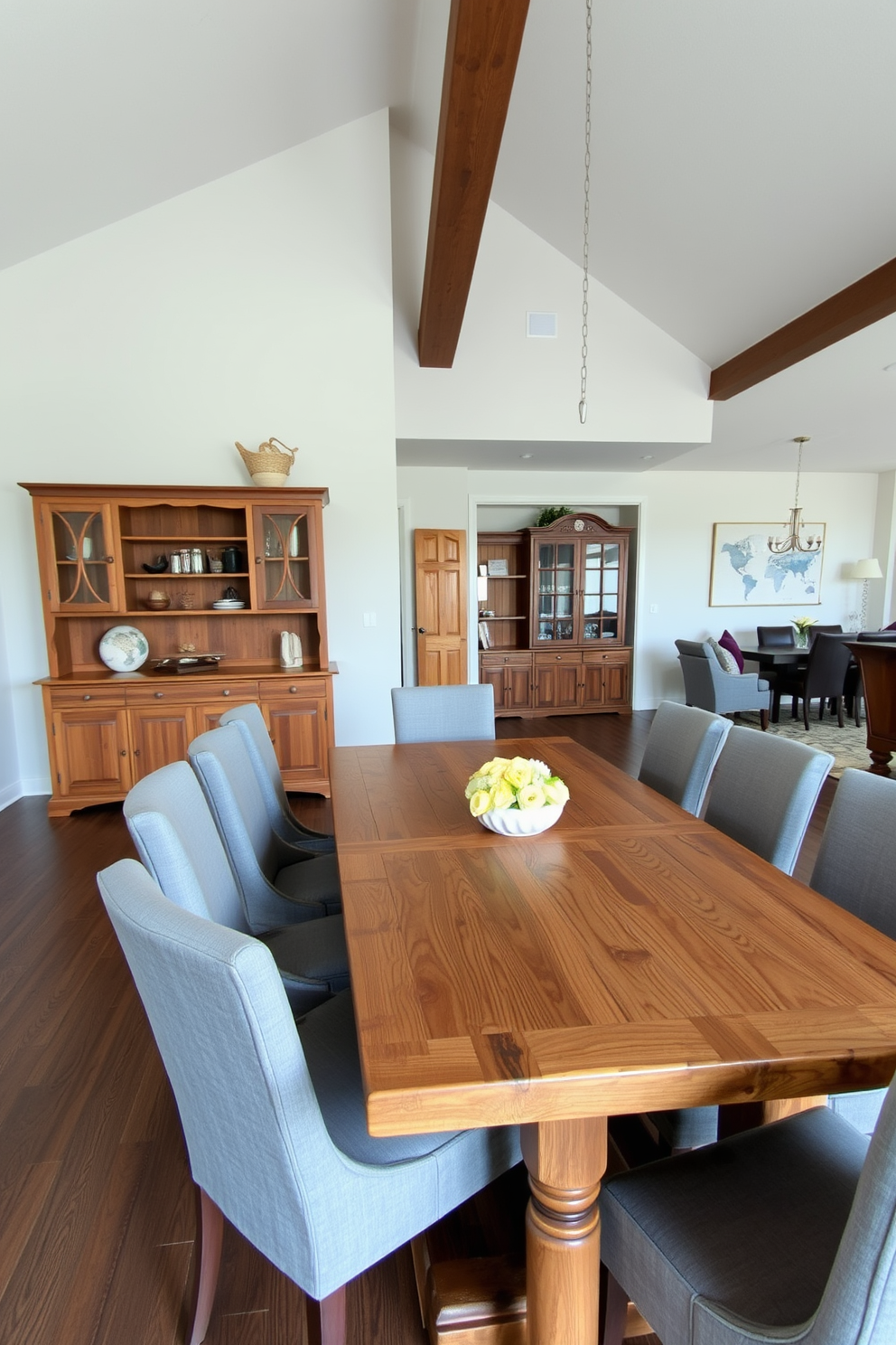 A contemporary dining room features a unique oval table made of reclaimed wood, surrounded by elegant upholstered chairs in a soft gray fabric. The space is illuminated by a stunning geometric chandelier that hangs above the table, creating a focal point in the open floor plan. Large windows allow natural light to flood the room, highlighting the neutral color palette of soft whites and warm beiges. A stylish area rug anchors the dining area, adding texture and warmth to the overall design.