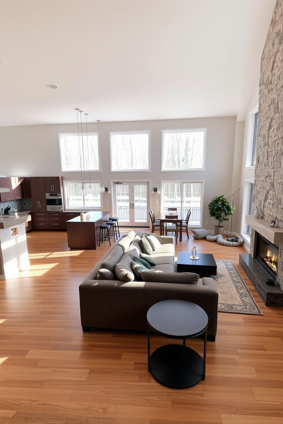 A seamless integration of kitchen and living room spaces creates an inviting atmosphere. The kitchen features a large island with bar seating, complemented by sleek cabinetry and modern appliances. In the living area, a cozy sectional sofa is positioned to face a contemporary fireplace. Large windows allow natural light to flood the space, highlighting the warm tones of the wooden flooring.