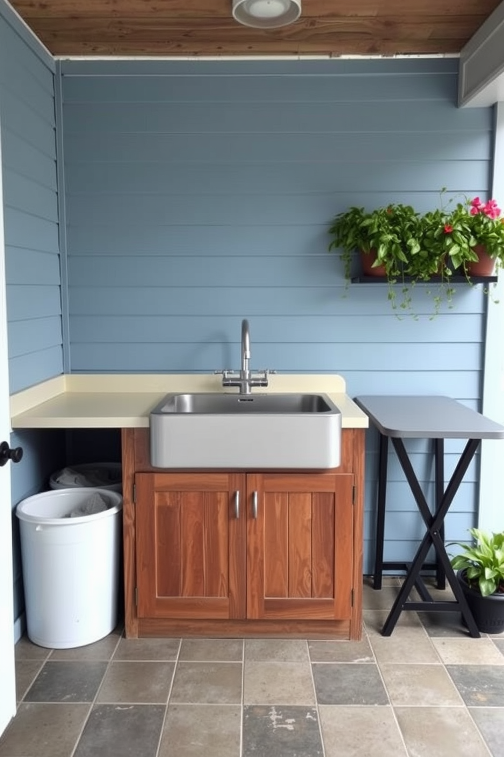 Utility sink with storage underneath. The outdoor laundry room features a spacious utility sink with a sleek faucet, complemented by a wooden cabinet below for ample storage. The walls are painted in a soft blue hue, and the flooring consists of durable, weather-resistant tiles. To the side, a folding table is set up for convenience, and potted plants add a touch of greenery to the space.