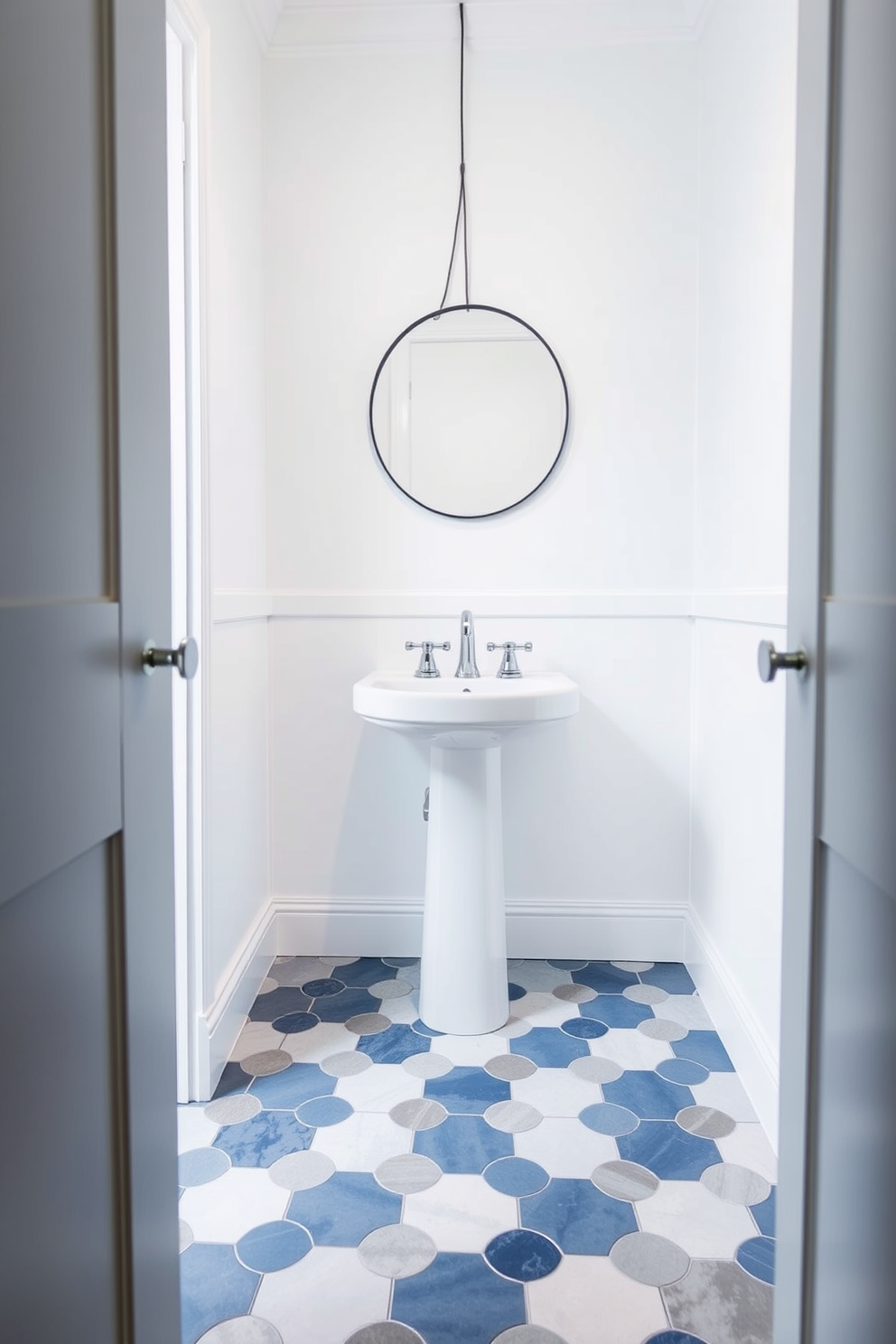 A stylish powder room featuring a floor adorned with striking hexagon tiles in varying shades of blue and gray. The walls are painted a soft white, creating a bright and airy atmosphere that complements the unique tile pattern. A sleek pedestal sink is positioned against one wall, accented by a modern chrome faucet. Above the sink, a round mirror with a thin black frame reflects the elegant tile work below.