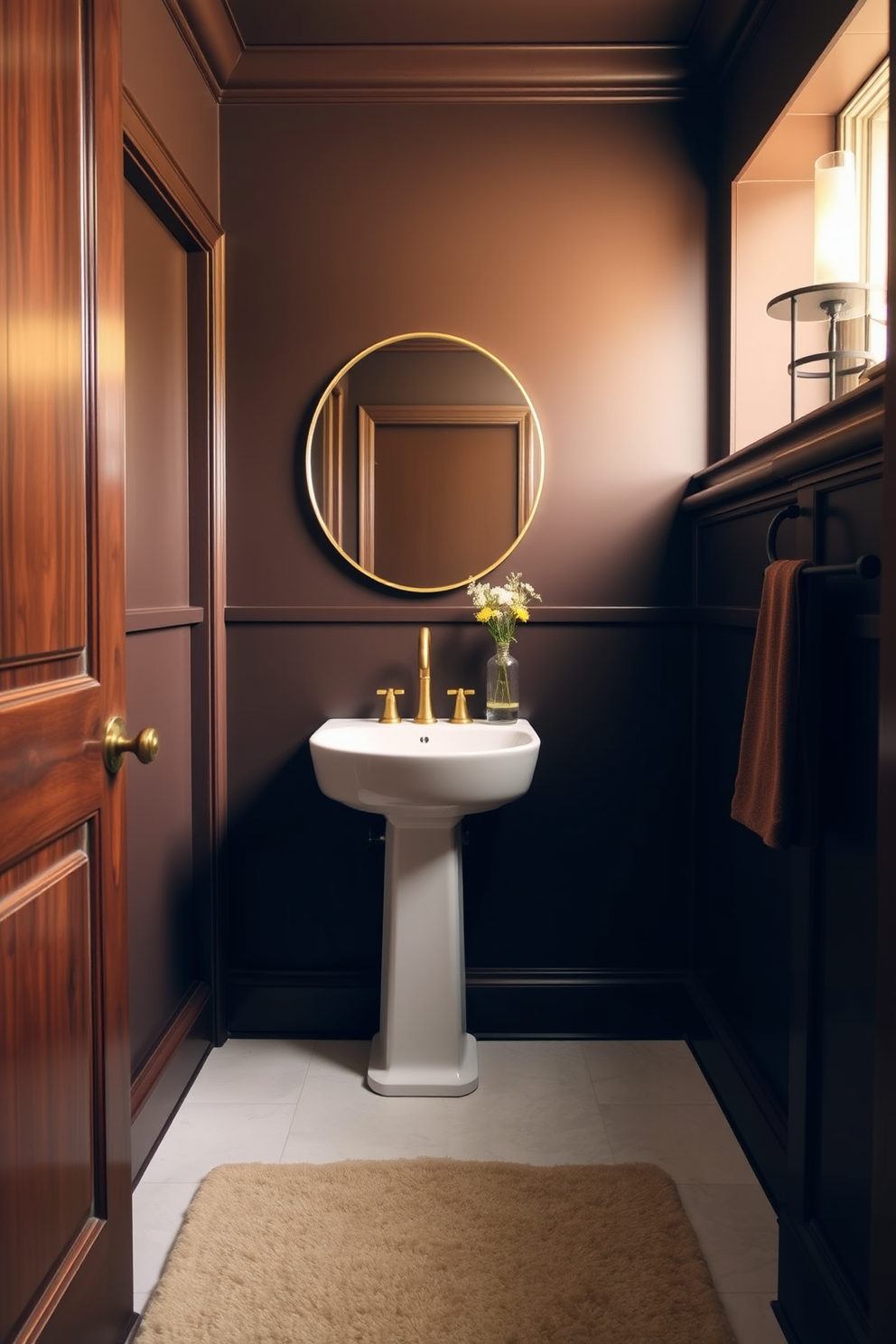 A warm chocolate brown powder room features rich wooden accents and soft ambient lighting. The walls are painted in a deep chocolate hue, creating an inviting and cozy atmosphere. A sleek white pedestal sink stands against the dark backdrop, complemented by a stylish gold faucet. A round mirror with a thin gold frame hangs above the sink, reflecting the warm tones of the space. The floor is adorned with light-colored tiles that contrast beautifully with the dark walls. A plush cream-colored rug adds softness underfoot, enhancing the room's warmth and elegance.