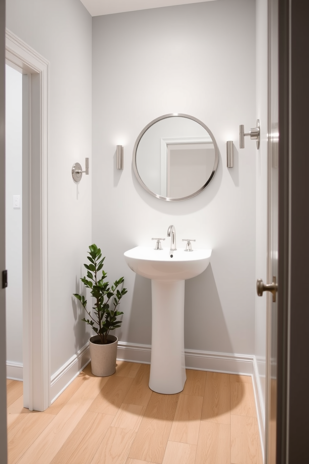 A chic powder room with light gray walls that create a modern and airy feel. The room features a sleek white pedestal sink and a stylish round mirror framed in brushed nickel. The flooring is a light wood that complements the gray tones, while a small potted plant adds a touch of greenery. Elegant wall sconces provide soft lighting, enhancing the contemporary atmosphere.