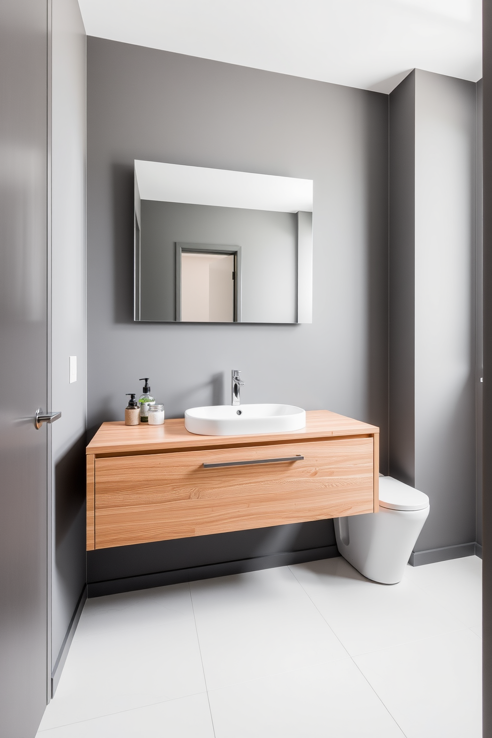 A modern powder room featuring a floating vanity with an integrated sink. The vanity is crafted from light oak wood, providing a warm contrast to the cool gray walls. Above the vanity, a sleek, frameless mirror reflects the soft ambient lighting. The floor is adorned with large white tiles, creating a clean and spacious feel.