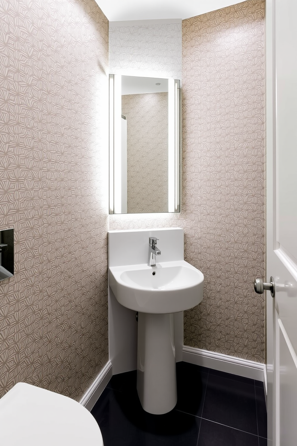 A modern powder room featuring a sleek sink with an illuminated mirror above it. The walls are adorned with elegant wallpaper in a subtle geometric pattern, and the floor is covered with polished dark tiles.