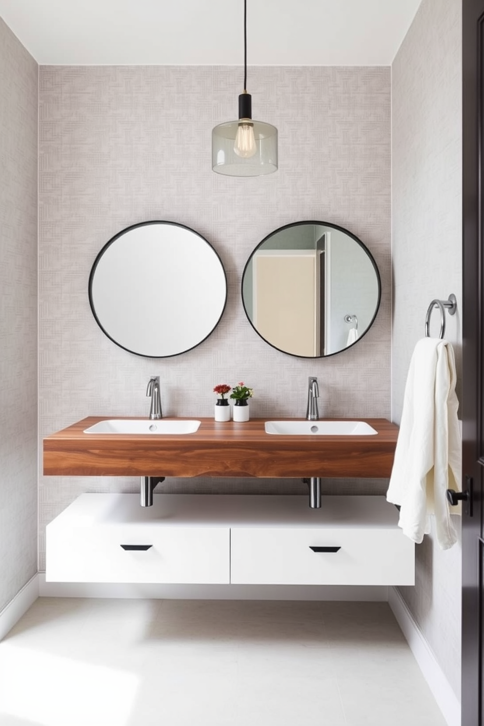 A stylish powder room features dual sinks integrated into a sleek floating vanity with a rich walnut finish. Above the vanity, a pair of round mirrors with minimalist black frames create a modern aesthetic. The walls are adorned with a soft gray wallpaper that adds texture and depth. A chic pendant light hangs from the ceiling, casting a warm glow over the space.