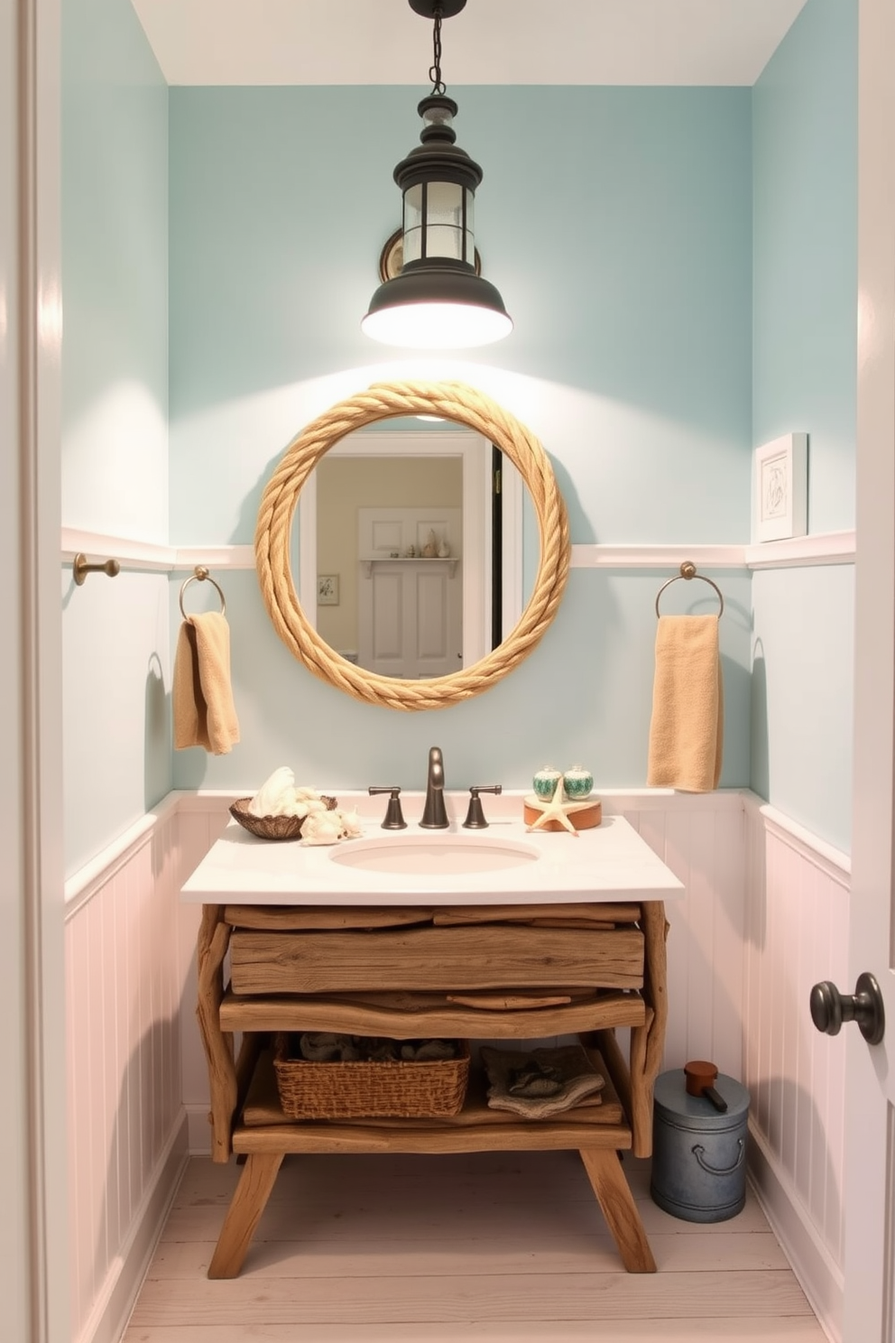 A charming powder room featuring a nautical theme vanity adorned with driftwood accents. The vanity is complemented by a round mirror framed with rope, and the walls are painted in a soft seafoam blue. Decorative elements include seashells and starfish arranged on the countertop, while a light fixture resembling a lighthouse hangs above. The floor is finished with whitewashed wood planks, enhancing the coastal ambiance of the space.