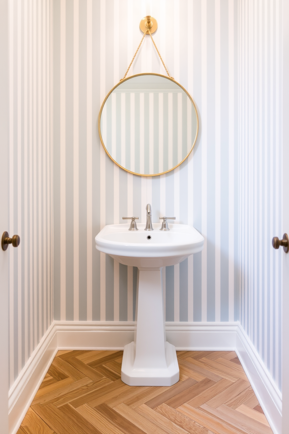 Classic stripes create a sense of timeless elegance in a powder room. The walls are adorned with vertical stripes in soft hues of cream and pale blue, complemented by a sleek white pedestal sink. A round mirror with a thin gold frame hangs above the sink, reflecting the stylish design. The floor features a herringbone pattern in light wood, adding warmth to the sophisticated space.