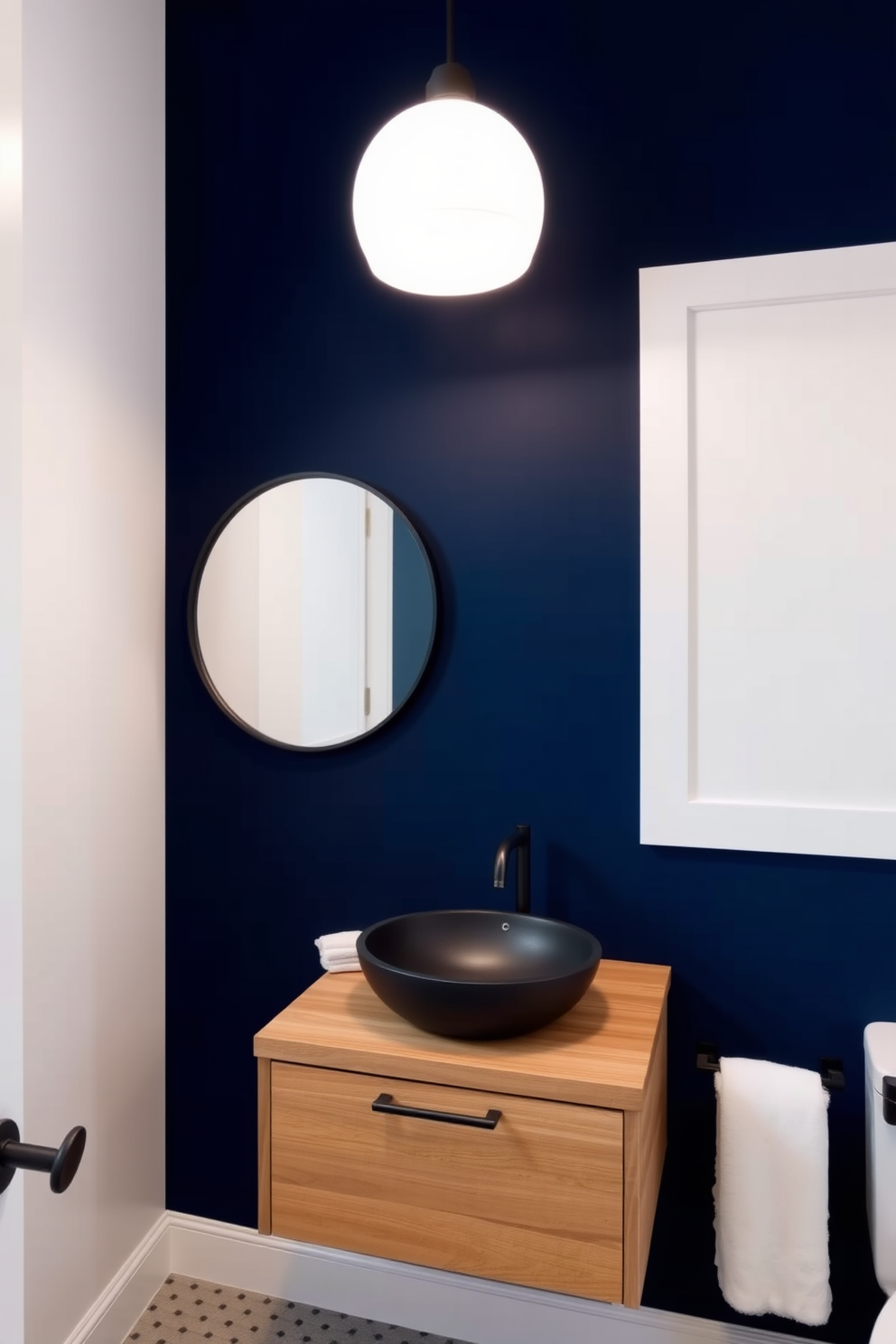 A bold accent wall in deep navy blue serves as the focal point of the quarter bathroom. The remaining walls are painted in a soft white, creating a striking contrast that enhances the space's elegance. A sleek, modern sink with a brushed nickel faucet is mounted on a floating wooden vanity. Above the vanity, a large round mirror with a black frame reflects the stylish decor of the room.