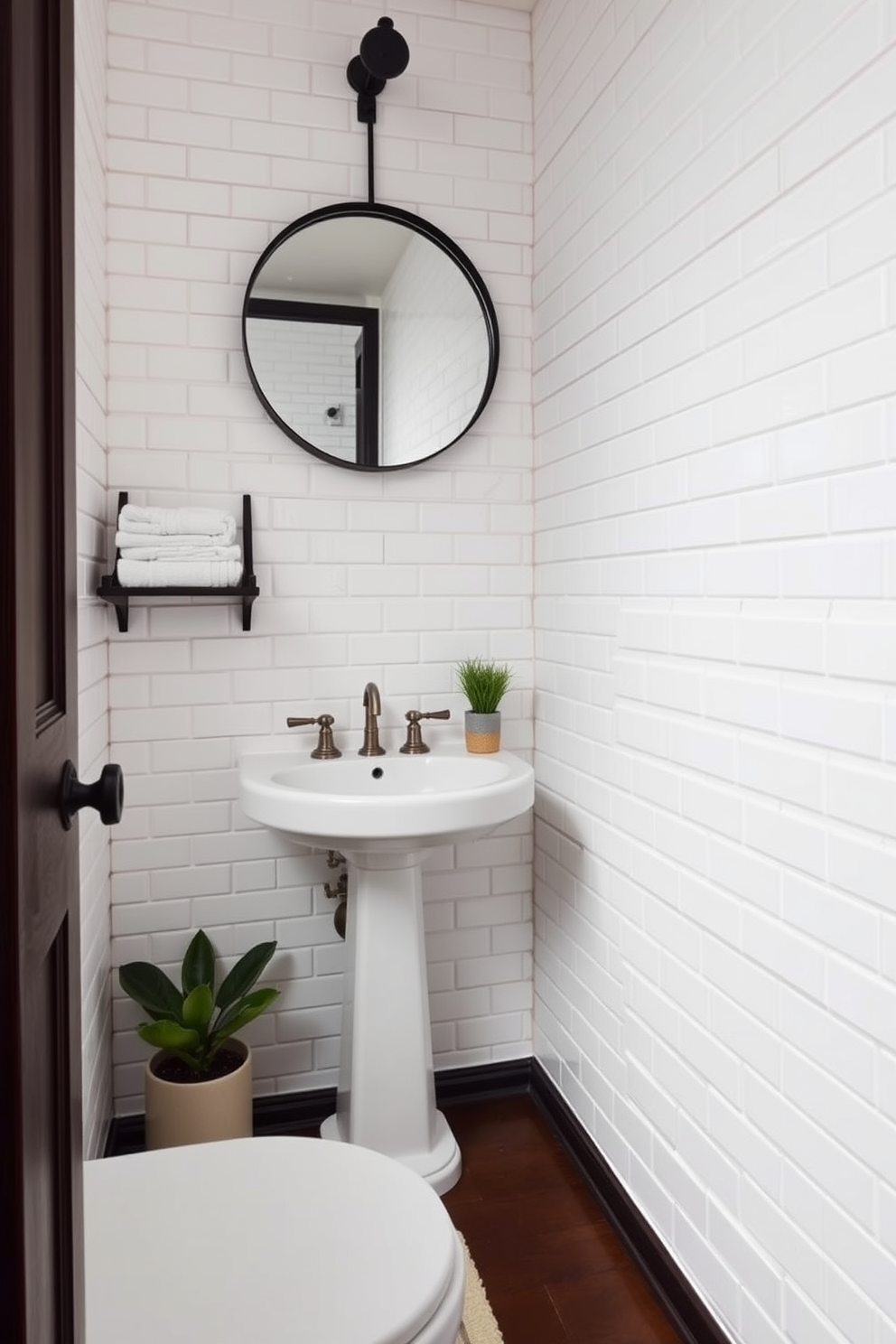 A quarter bathroom featuring classic subway tiles in a crisp white finish. The walls are adorned with these tiles, creating a timeless and clean aesthetic that enhances the small space. A sleek pedestal sink is positioned against the wall, complemented by a vintage-style faucet. Above the sink, a round mirror with a simple black frame reflects the elegant design. The floor is finished with dark hardwood, adding warmth and contrast to the bright tiles. A small shelf holds neatly folded towels, while a potted plant adds a touch of greenery to the decor.