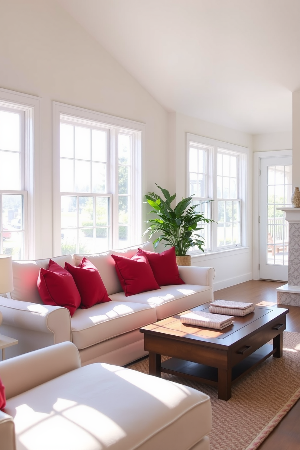 A cozy living room featuring a white sofa adorned with vibrant red throw pillows. The space is illuminated by natural light streaming through large windows, creating a warm and inviting atmosphere.