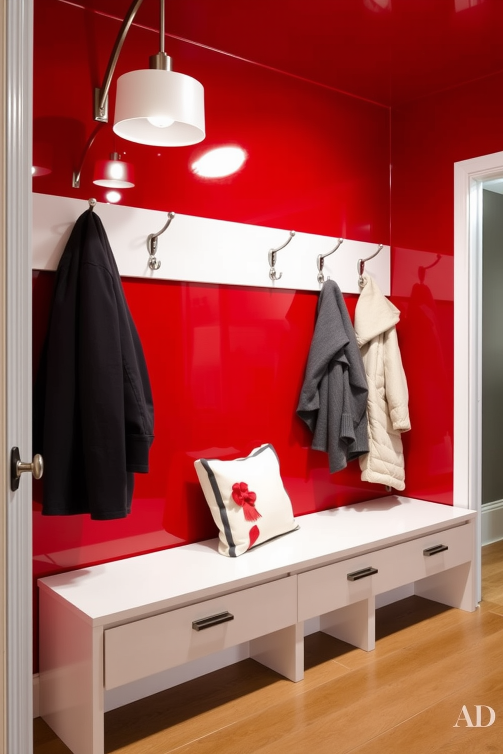 A modern mudroom featuring glossy red paint on the walls creates a vibrant and inviting atmosphere. The space includes a sleek bench with storage underneath and hooks for coats, all accented by stylish lighting fixtures.