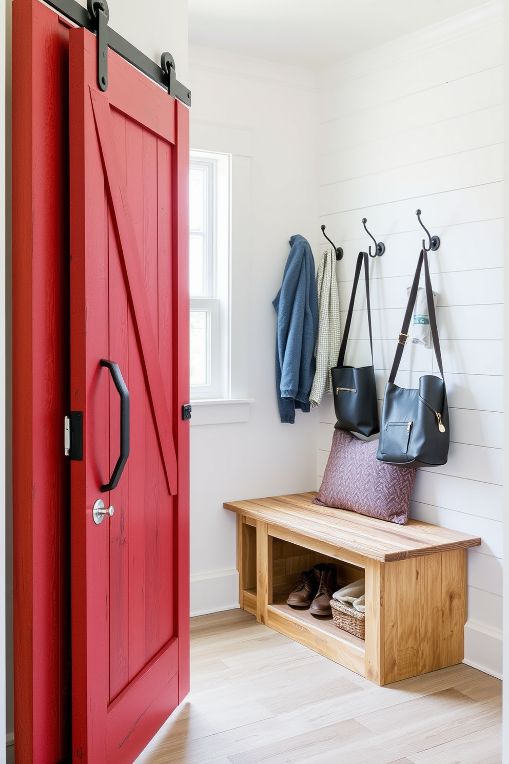 A rustic red barn door serves as the entrance to a cozy mudroom. Inside, the space features a bench made of reclaimed wood with built-in storage underneath for shoes and gear. The walls are adorned with shiplap in a soft white hue, providing a bright contrast to the rich red door. Hooks made of wrought iron are mounted on the wall for hanging coats and bags, adding a charming farmhouse touch.