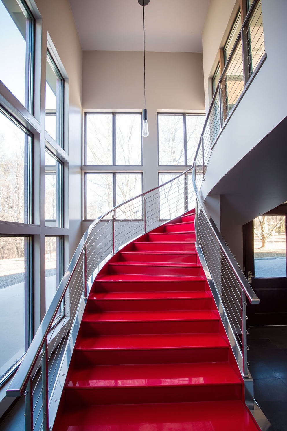 A sleek red staircase with stainless steel accents gracefully curves upward, creating a striking focal point in the entryway. The polished stainless steel railings complement the vibrant red steps, enhancing the modern aesthetic of the space. Surrounding the staircase, large windows allow natural light to flood in, illuminating the bold color and sleek materials. The minimalist design is further accentuated by a simple yet elegant pendant light hanging above the staircase.