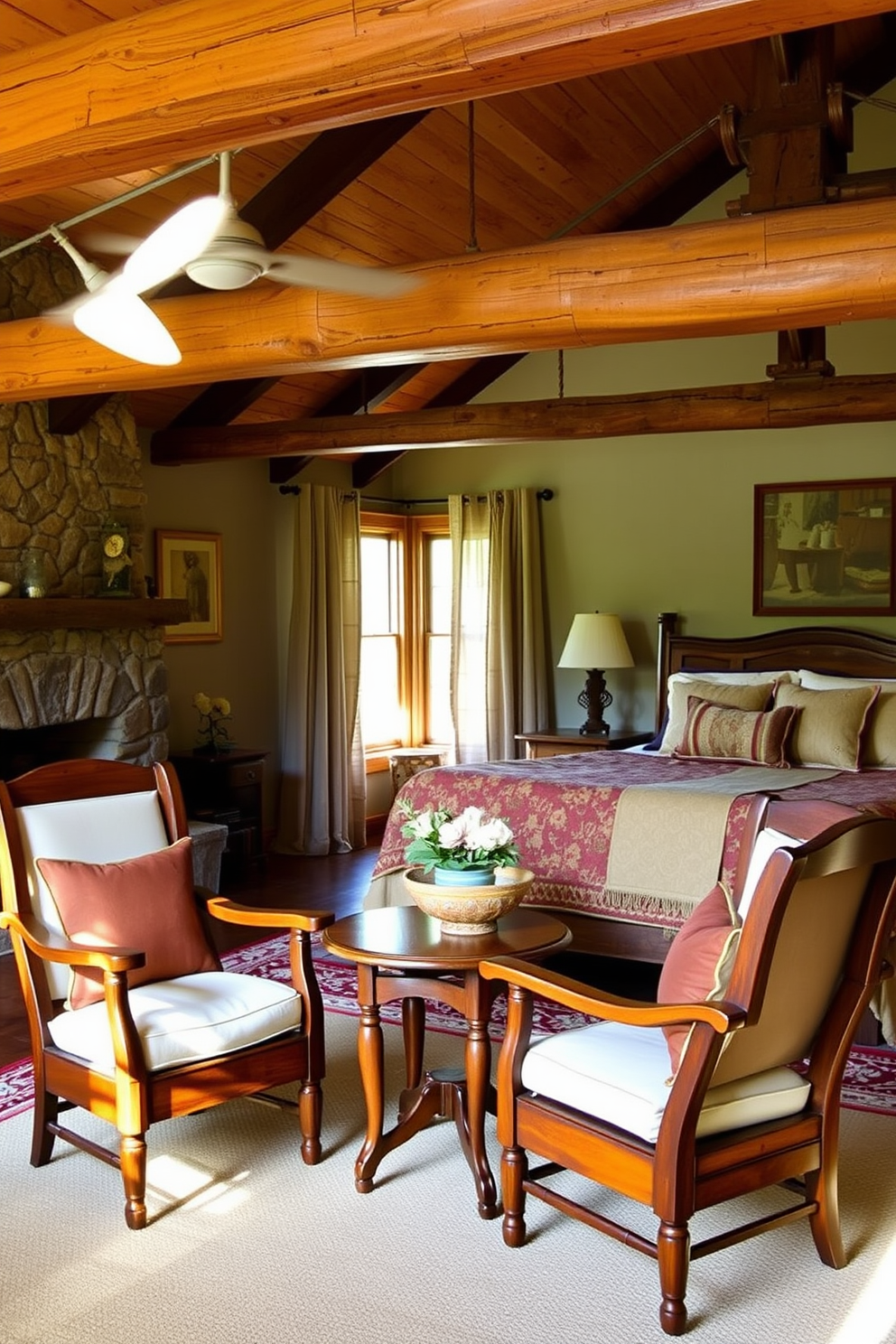 Wooden accent chairs with plush cushions are arranged around a small, round wooden table in a rustic bedroom setting. The room features exposed wooden beams, a stone fireplace, and warm earth tones throughout the decor. A large, inviting bed with a handmade quilt sits against a wall adorned with vintage artwork. Natural light streams in through a pair of sheer curtains, enhancing the cozy ambiance of the space.