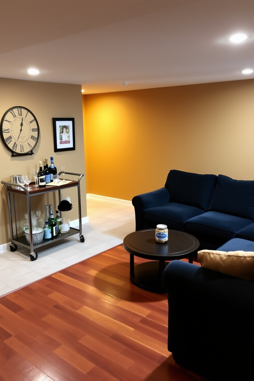 A cozy basement space designed for relaxation and entertainment. The walls are painted in a warm beige tone, and the flooring is a rich hardwood that adds warmth to the area. In one corner, a stylish bar cart is set up with an assortment of glasses and bottles, perfect for easy entertaining. A plush sectional sofa in a deep navy blue is paired with a round coffee table, creating an inviting atmosphere for gatherings.