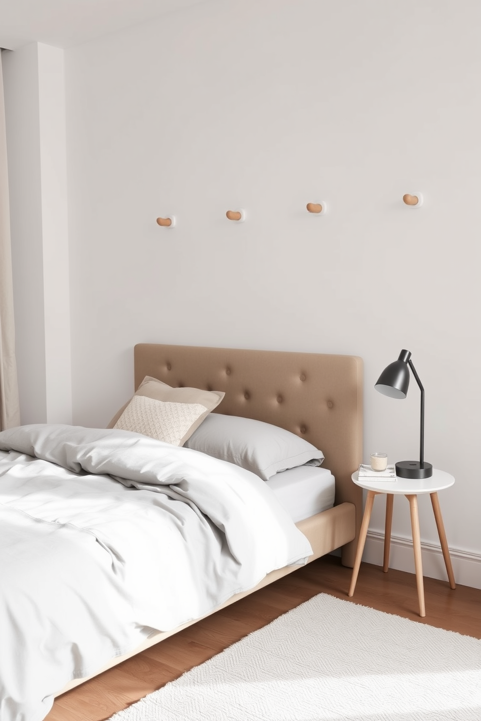 A minimalist bedroom featuring simple wall hooks for easy organization. The hooks are made of natural wood and are mounted on a soft white wall, providing a functional yet stylish touch. The bedroom is designed with a neutral color palette, including a plush bed adorned with light gray linens. A small bedside table holds a modern lamp, while a cozy rug anchors the space, creating a serene atmosphere.