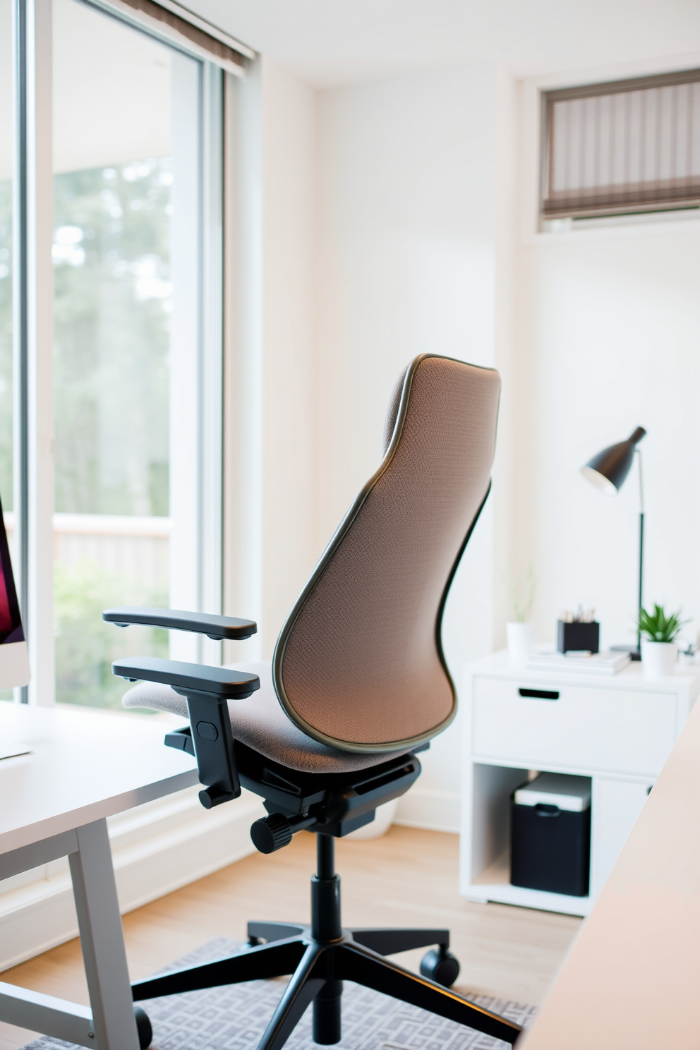 An ergonomic chair designed for optimal comfort and support features adjustable height and lumbar support. The chair is upholstered in soft fabric and includes armrests to enhance relaxation during long hours of work. The simple home office design emphasizes minimalism with a clean desk and organized workspace. Natural light floods the room through large windows, complemented by a neutral color palette for a calming atmosphere.