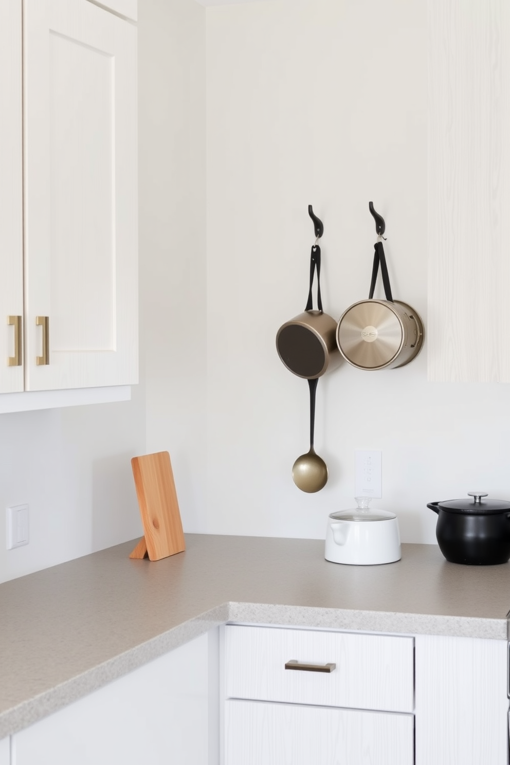 A simple kitchen design featuring functional wall hooks for easy access to utensils and pots. The cabinetry is a soft white with a light wood finish, and the countertops are a durable quartz in a subtle gray tone.