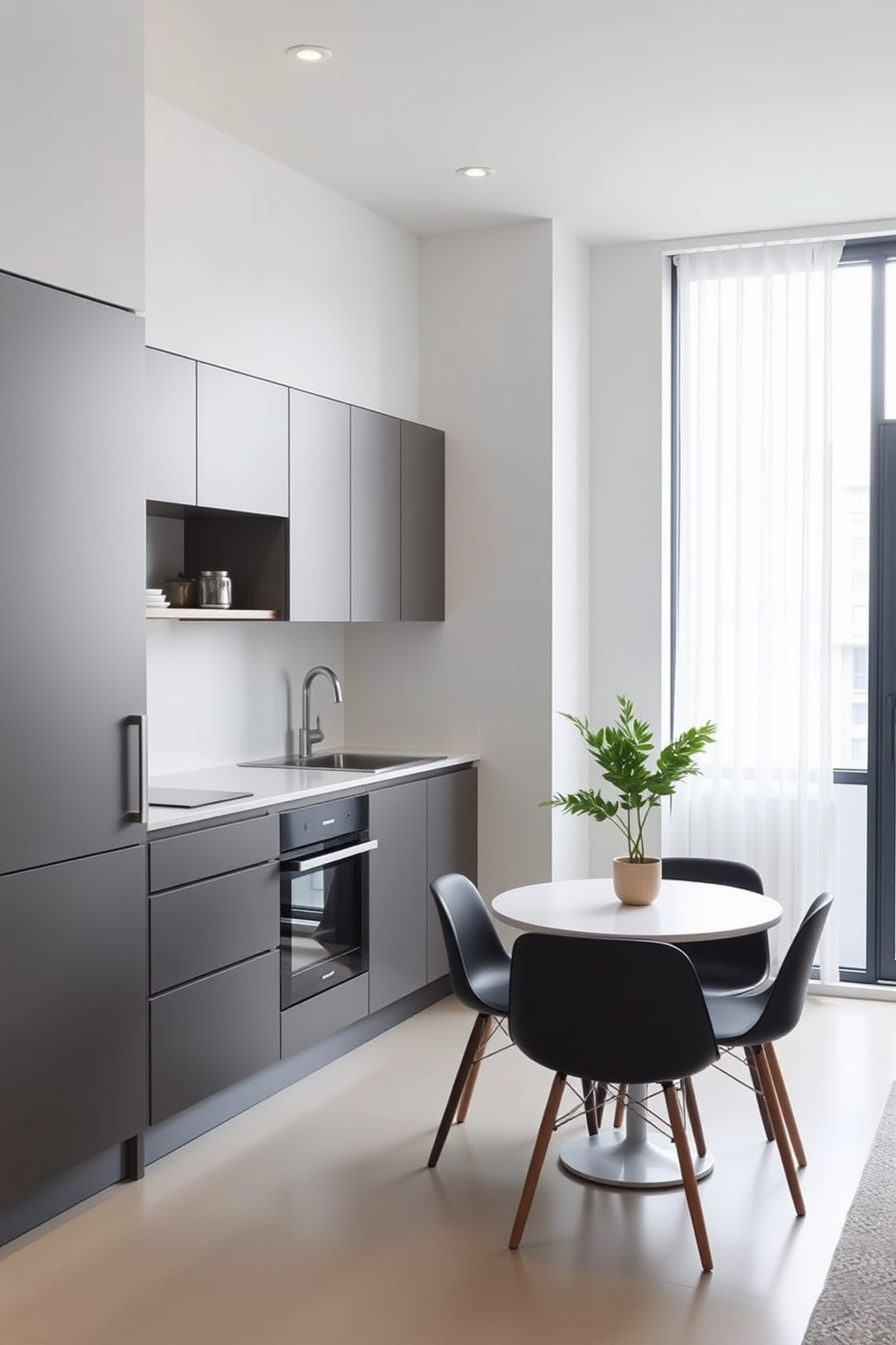 A minimalist kitchen design in a small apartment featuring sleek cabinetry with a matte finish. The countertops are white quartz, and a compact dining table with two chairs is positioned near a large window for natural light.