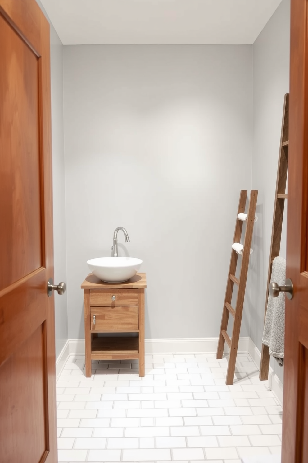 A cozy small bathroom with a sleek design. The walls are painted in a soft light gray, and the floor is covered in white subway tiles. A compact wooden vanity with a vessel sink sits against one wall. A small ladder for towels leans against the opposite wall, adding a touch of warmth and functionality.