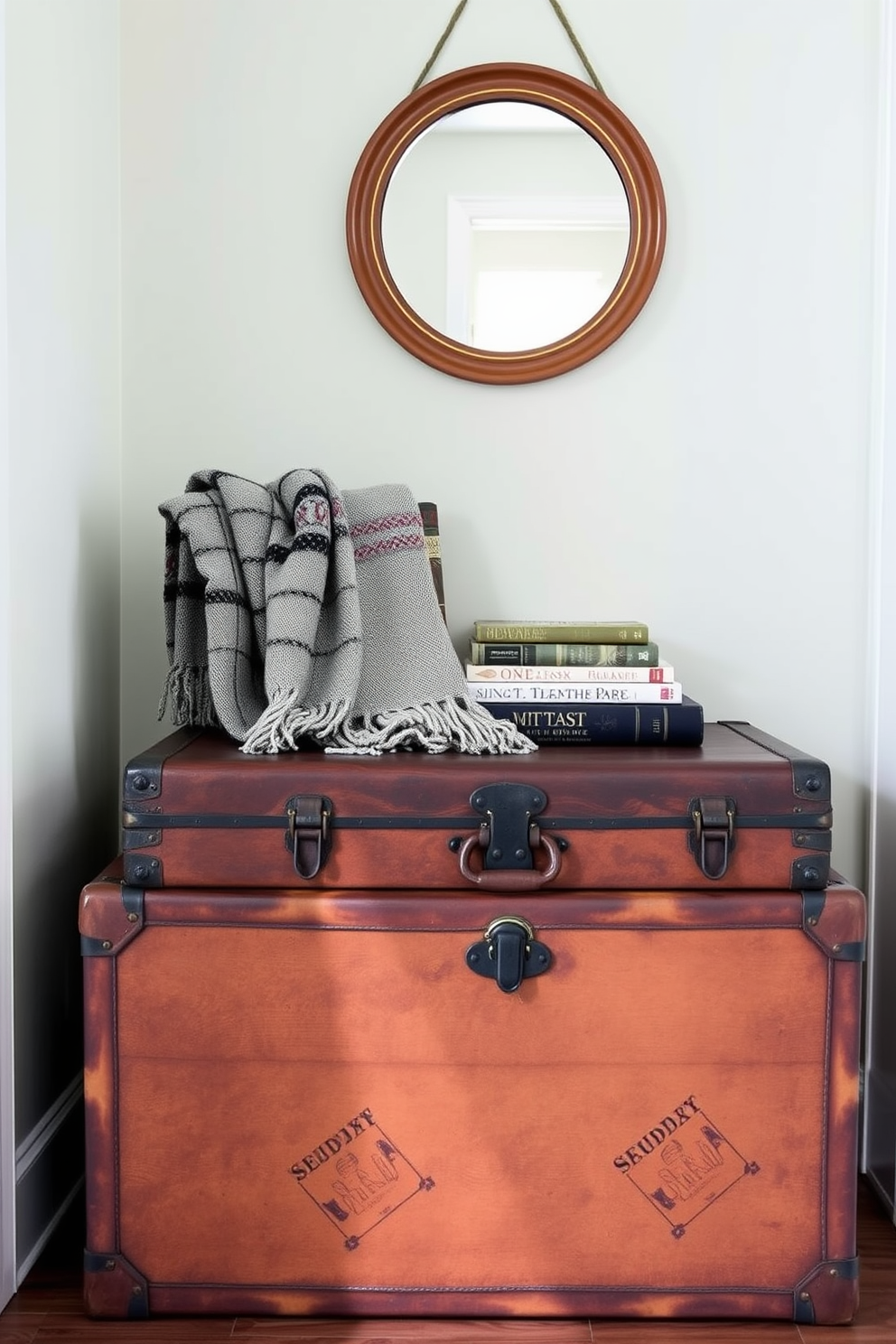 A vintage trunk serves as a unique storage solution in a small entryway. The trunk is placed against the wall, adorned with a decorative throw blanket and a few travel-themed books on top. The walls are painted in a soft pastel hue, complementing the warm wood tones of the trunk. A small round mirror hangs above the trunk, creating an inviting focal point and enhancing the sense of space.