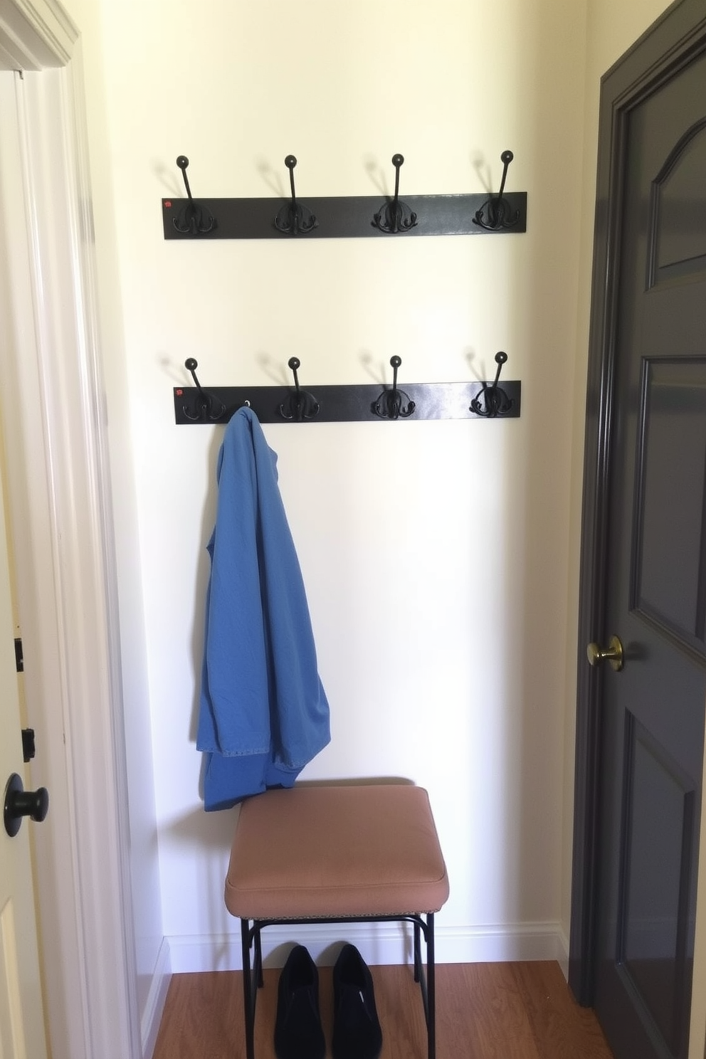 A small entryway features wall-mounted coat hooks arranged neatly on a light-colored wall. Below the hooks, a compact bench with a cushioned seat provides a comfortable spot for putting on shoes.