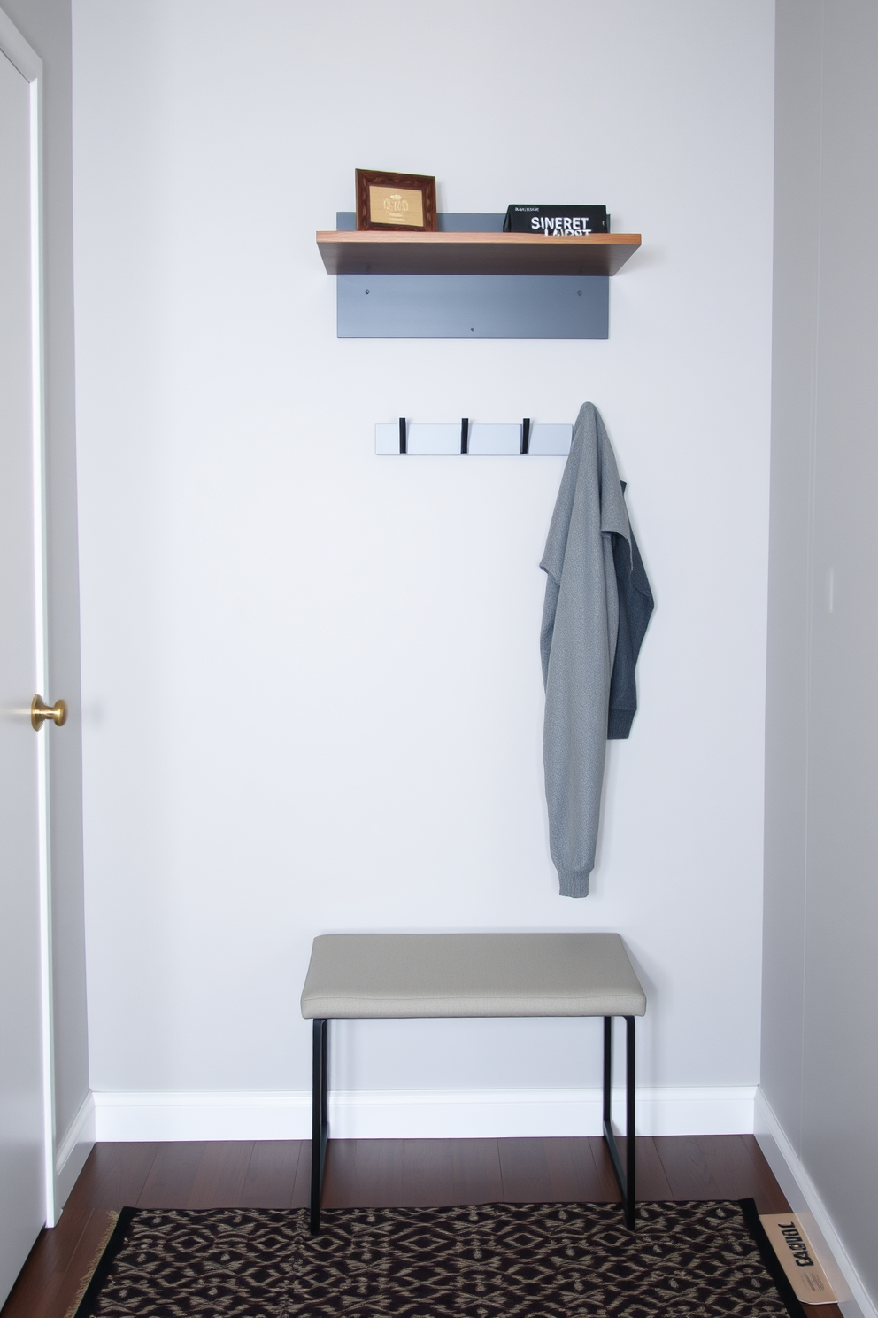 A sleek coat rack with a modern design stands against a light gray wall in a small entryway. The floor is adorned with a geometric patterned rug, and a minimalist bench sits below a stylish wall-mounted shelf for added storage.