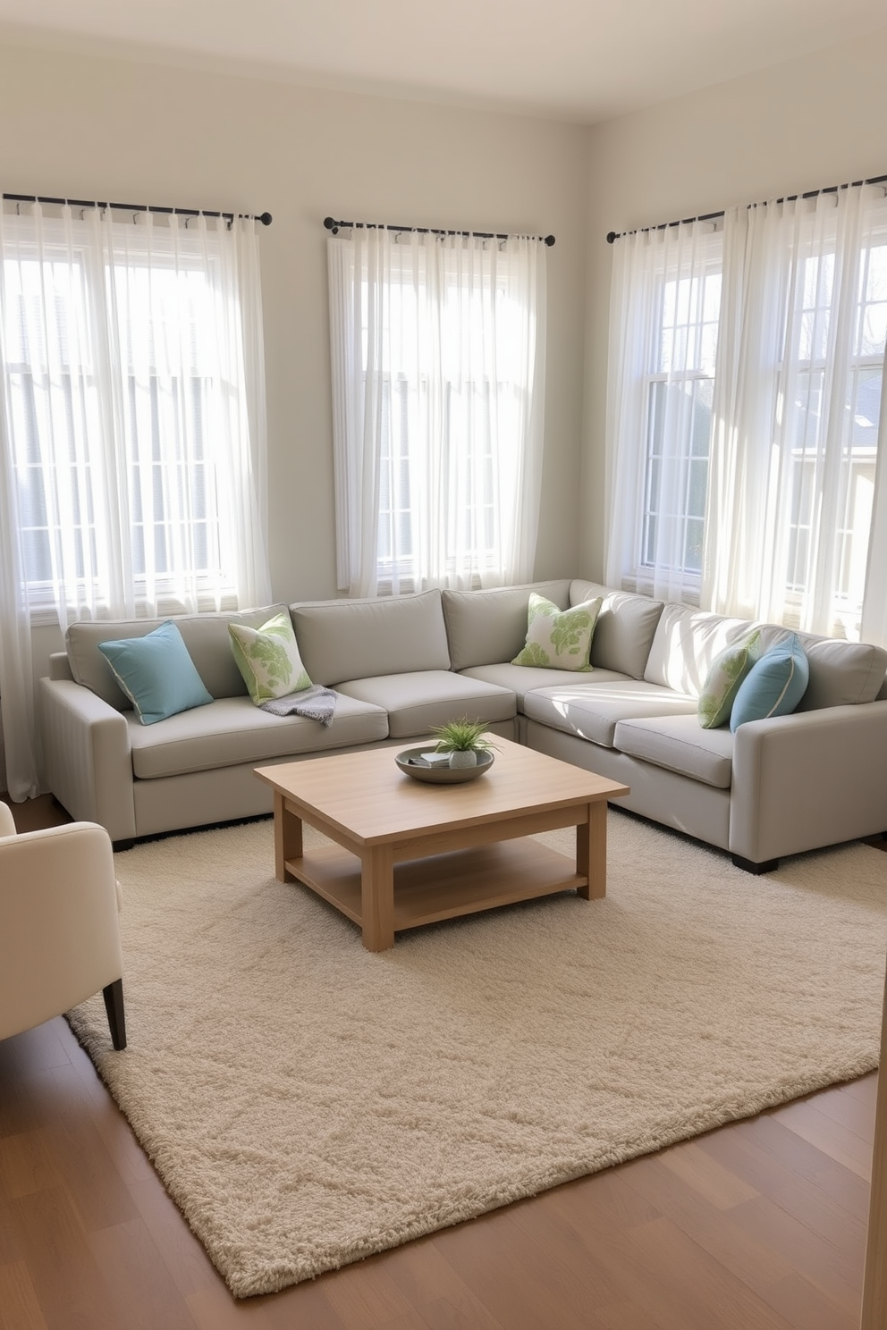 A cozy family room featuring soft beige walls and a light gray sectional sofa that invites relaxation. Natural light floods the space through large windows adorned with sheer white curtains, enhancing the airy atmosphere. A light wood coffee table sits in the center, surrounded by a plush area rug in subtle pastel hues. Decorative pillows in soft blues and greens add a touch of color while maintaining the serene feel of the room.