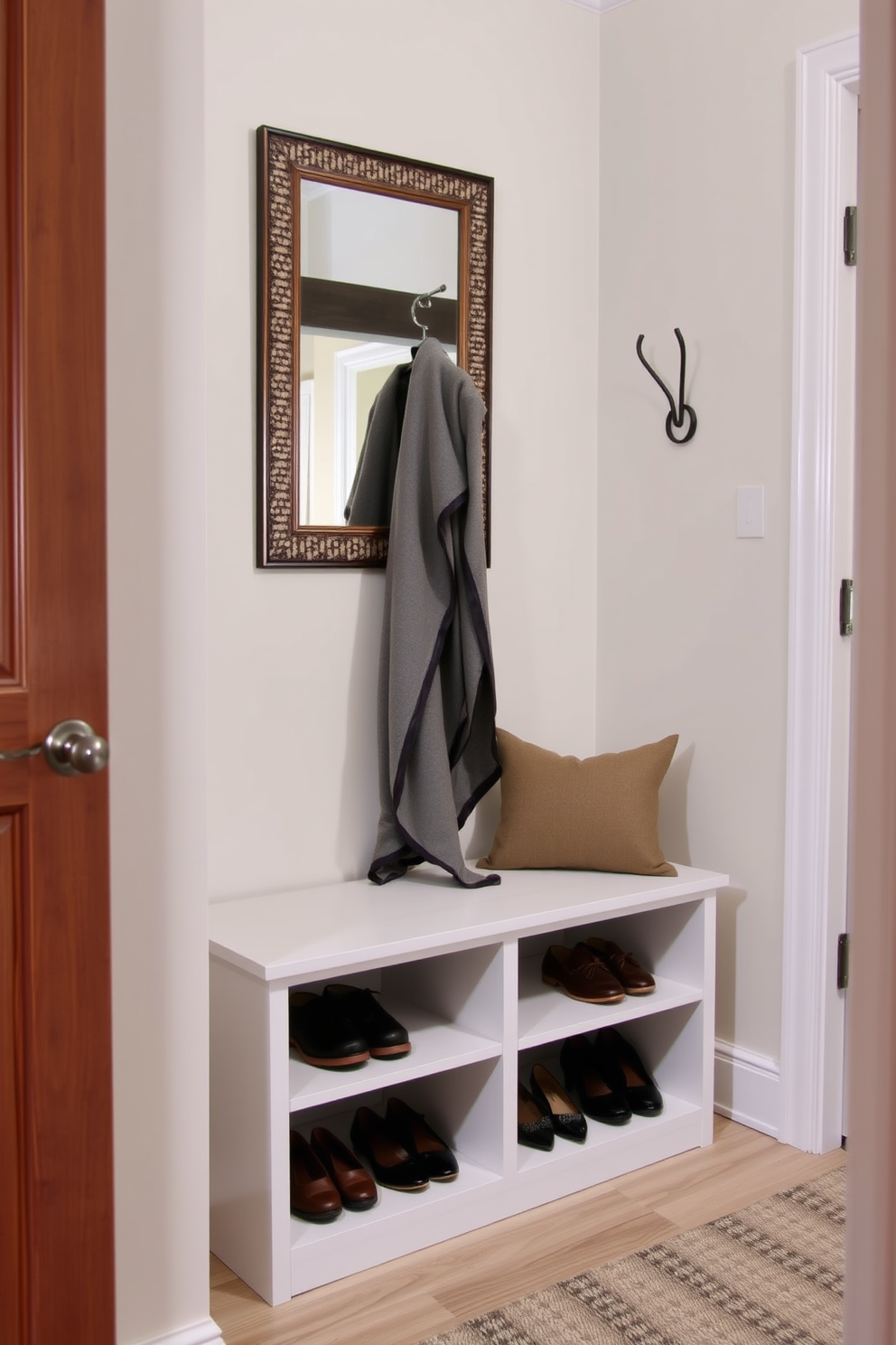 A small foyer features a sleek bench with under-bench storage designed to neatly organize shoes. The walls are adorned with a soft neutral color, complemented by a stylish coat rack and a decorative mirror above the bench.