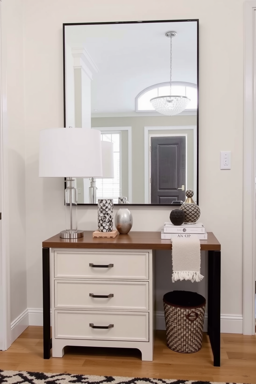 A stylish foyer featuring a small console with drawers positioned against the wall. The console is adorned with decorative items and a sleek lamp, while a large mirror hangs above it, reflecting the inviting space.