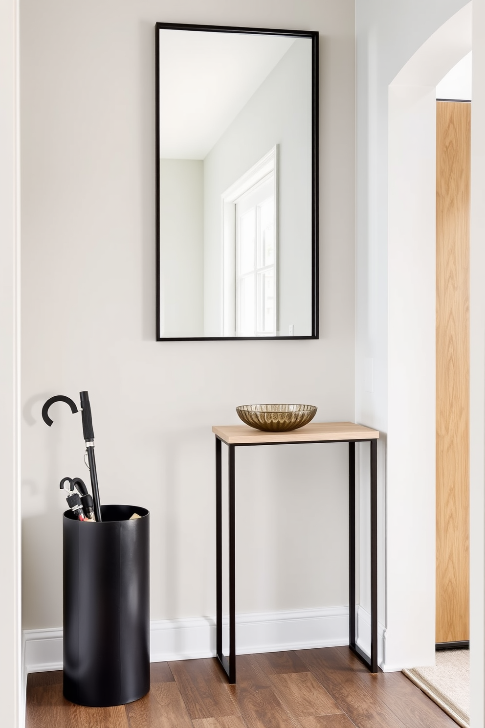 A stylish umbrella stand made of sleek metal with a matte black finish sits elegantly in the corner. The stand features a minimalist design that complements the overall aesthetic of the foyer while providing practical storage for umbrellas. The foyer is adorned with a small console table in a light wood finish, topped with a decorative bowl for keys. A large mirror hangs above the table, reflecting natural light and creating an inviting atmosphere.